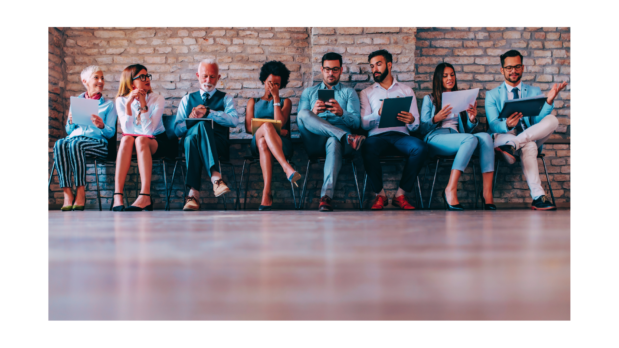 8 people of assorted ages, ethnicities, and genders sit in waiting room chairs as though waiting on an interview. All are dressed in summery business attire.